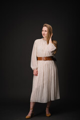 Young serious luxury woman isolated on black wall with copy space. Beautiful girl with hand near head looking at camera. Portrait of lady in long dress looks confident on black background. Photo.