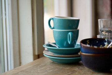 Two sets of used dishes with green cappuccino cups on wooden counter