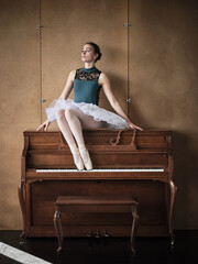 Slender ballerina in tutu and pointe shoes sitting on piano