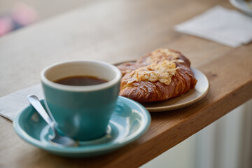 cup of coffee and almond croissant on a wooden table