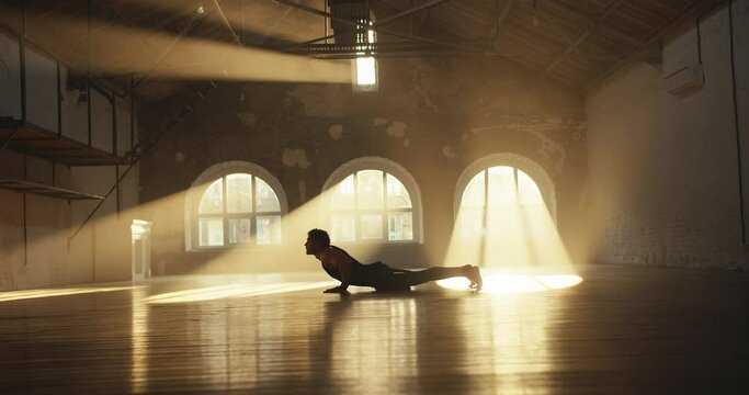 A man in a black summer sports uniform does a Cat Stretch Pose in the Sun Room. The rays of the sun paint the hall in golden colors