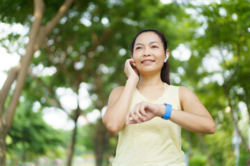Beautiful smart and good looking Asian adult woman checking on a smartwatch or fitness tracker while practicing running - jogging at the park.