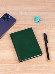 Design concept - top view of  green notepad with phone, bookmarks, binder and pen on wooden table