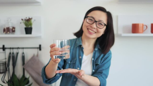 Slim female holding beverage in hand on kitchen background