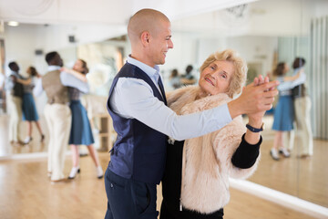 Elderly woman learning ballroom dancing movements in pair - obrazy, fototapety, plakaty
