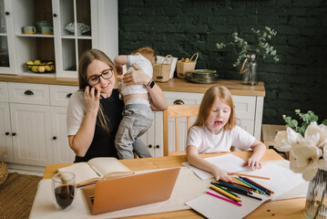 Angry and tired mother working with kids at home. Woman working, learns on laptop computer....