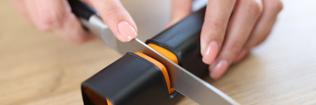 Woman hands sharpen knife with sharpener on kitchen table close-up.