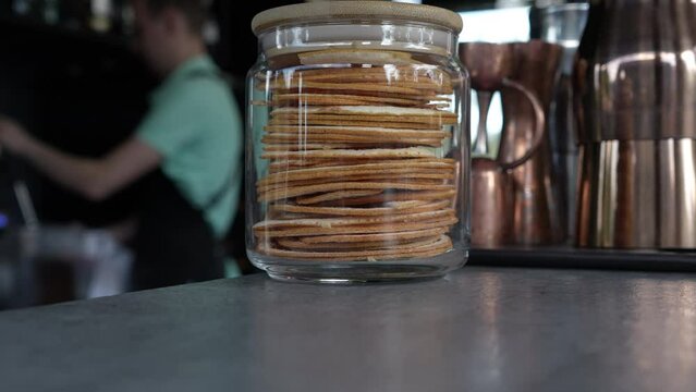 A jar of cookies on a bar close-up. In the background, the bartender is out of focus.