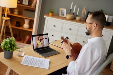 A female student learning from a music teacher to play the violin online using a laptop. - Powered by Adobe