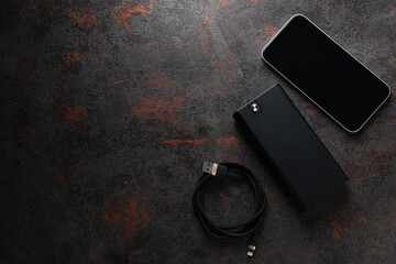Powerbank, smartphone and cord on dark gray background, space for text