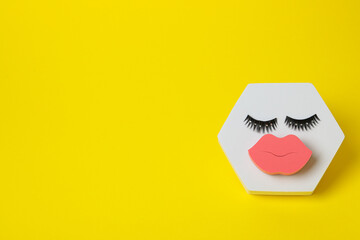 Cosmetic sponge and false eyelashes on yellow background, space for text