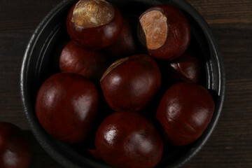 Obraz premium Brown chestnut fruits in a black bowl on a dark background