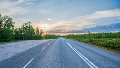 Asphalt road in tundra landscape with low trees during beautiful sunset