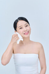 아시아 한국의 검은머리의 젊은 여자 모델이 끈 나시를 입고 흰색 마사지기구를 얼굴 목 어깨에 대고 포즈를 취하고 있다.   