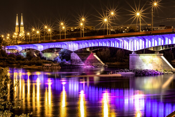 Bridge over the river illuminated by blue and purple neon at night. The Slasko-Dabrowski bridge over the Vistula river, Warsaw, Poland