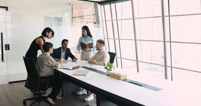 Five multinational young and mature teammates working use laptop review sales stats result, forecasting, share solution, develop marketing plan in boardroom, doing paperwork, learn financial charts