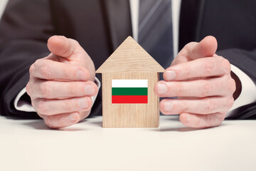 Businessman hand holding wooden home model with Bulgarian flag. insurance and property concepts