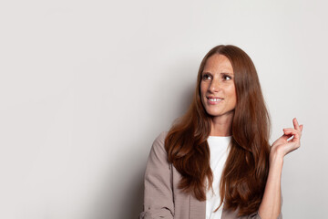 Naklejka premium Pretty positive woman looking up and holding empty hand against white studio wall background