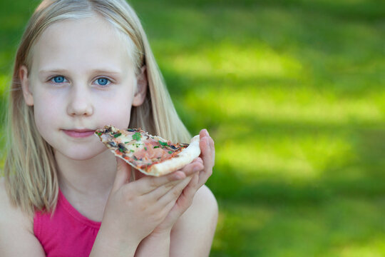 Young beautiful blonde girl eating pizza outdoor on green background