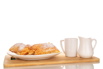 Three aromatic puff pastry buns with apples on a white ceramic plate with a white cup and milk jug, macro, isolated on white background.