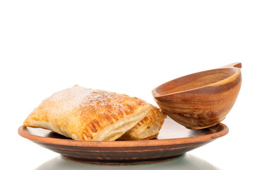 Two aromatic puff pastry buns with apples on a clay plate with a wooden cup, macro, isolated on a...
