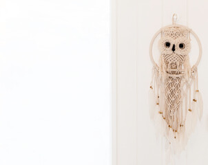 A beautiful hand made bohemian dreamcatcher with a crochet Owl and white feathers hanging on a white door with light coming from the window on the left. - obrazy, fototapety, plakaty