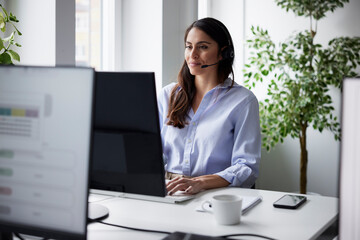 Smiling mid adult businesswoman using headset in office in front of computer screen