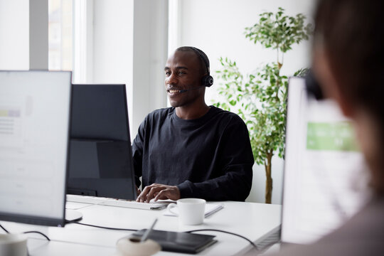 Smiling mature businessman using headset and desktop PC in office