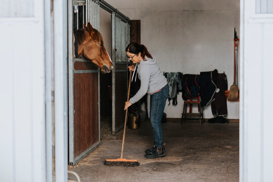 Woman in stable sweeping floor