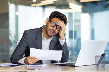 Upset and disappointed businessman financier investor looking at camera, man holding papers reports...