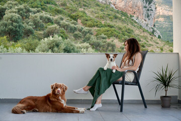 a girl on chair and two dogs are relaxing on the terrace. Jack Russell Terrier and Nova Scotia Duck...