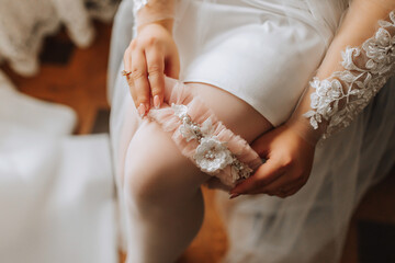 The bride in a white robe wears a beige garter on her leg. Tender morning of the bride.