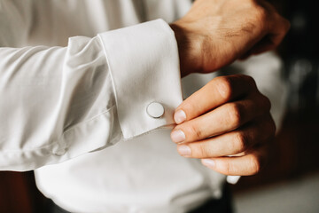 The groom fastens the cufflinks at the wedding reception with a large plon. The man wears a white...