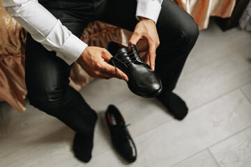 a man in a white shirt, lacing black shoes and preparing to meet his bride. The man wears classic...