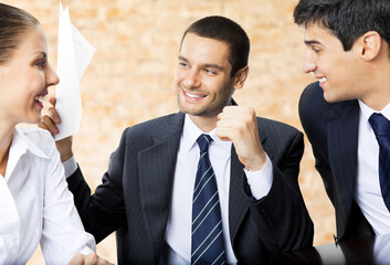 Happy smiling successful gesturing businessman with document and colleagues at office.  Brown bricks wall background.