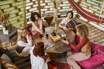 Obraz premium multiethnic boho style girlfriends at wooden table with tarot cards and tea in retreat center
