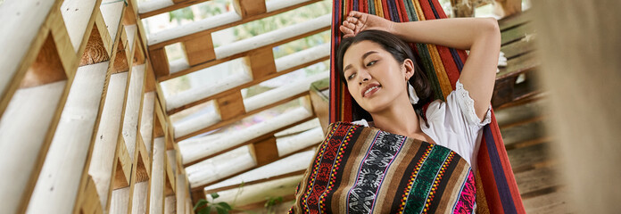 Fototapeta na wymiar pleased woman in boho style clothes resting in hammock, retreat, harmony, rejuvenation