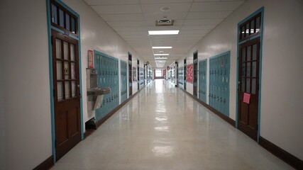 Wide angle view looking down a long empty high school hallway with US American flag with corridor...