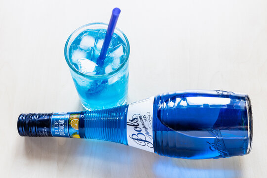 Moscow, Russia - August 2, 2022: above view of lying blue Curacao liqueur made by Bols distillery, founded in 1575 in Amsterdam, on pale table and glass with drinking straw and Blue Lagoon cocktail