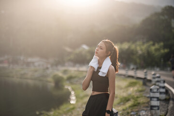 Portrait Young beautiful Asian woman wiping sweat after evening jogging in the park.