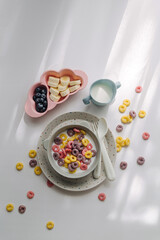 Colorful cereal rings with milk in bowl. Dry children's breakfast. Cute children's plates and bowls with tasty food. Creative serving for baby. Concept of kids menu, nutrition and feeding.