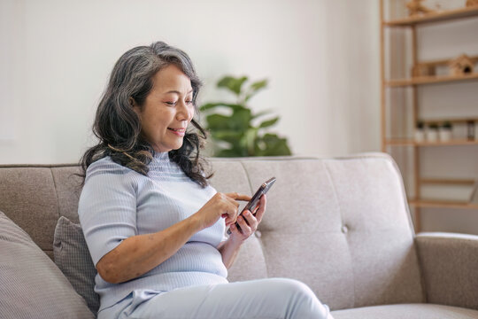 Portrait, Happy 60s retired Asian woman using her phone on a sofa in the living room. chatting, scrolling on the phone