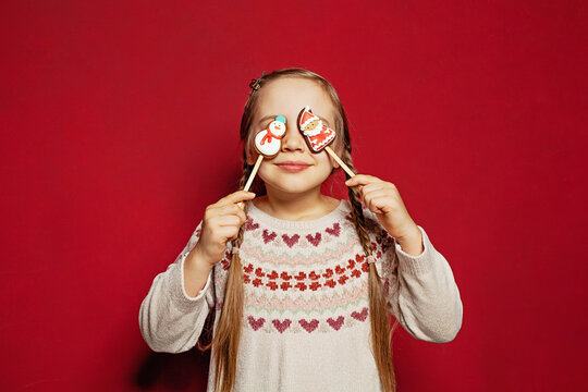 Cute funny little girl closing her eyes with gingerbread on red background