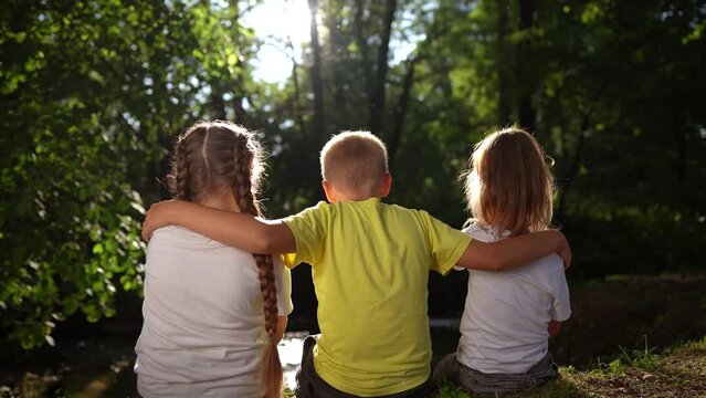 children sit on the banks of the river. happy family childhood dream concept. a group of little children sit together by the river and talk. kids spend time outdoors lifestyle in nature in the forest