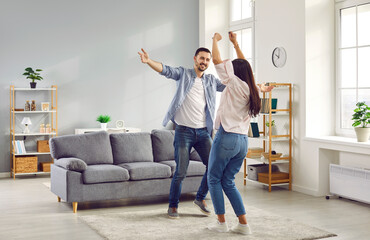 Happy family couple having fun together and dancing in the living room at home. Young man and woman...