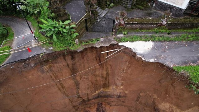 The edge of break and leaky subak system channel, aftermath of local landslide. camera rotates slowly, showing details and ruined road. stone fence of house compound looms over dangerous abyss