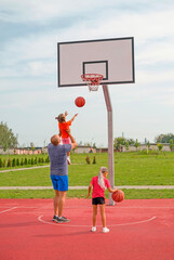 The father lifts the little girl high up, helping her to throw the ball into the basketball basket....