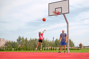 A small child throws a basketball into the basket making a powerful jump. The father watches the...