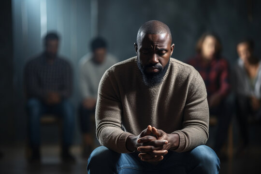 Sad anxiety depressed black man at support group meeting for mental health and addiction issues in anonymous community space with many people around