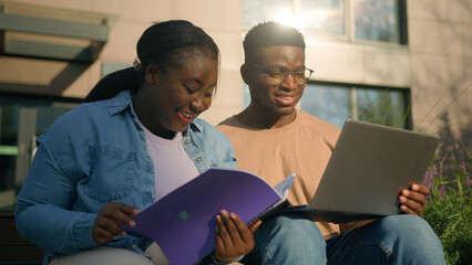 Two friends African American ethnic students woman man girl guy discuss homework university prepare for exams together with computer talking in city studying education with laptop study book outdoors